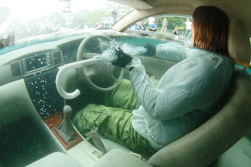 浸水した車の窓ガラスを破る女性