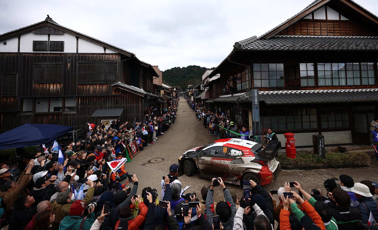 日本らしい町並みの中を走行するラリーカー