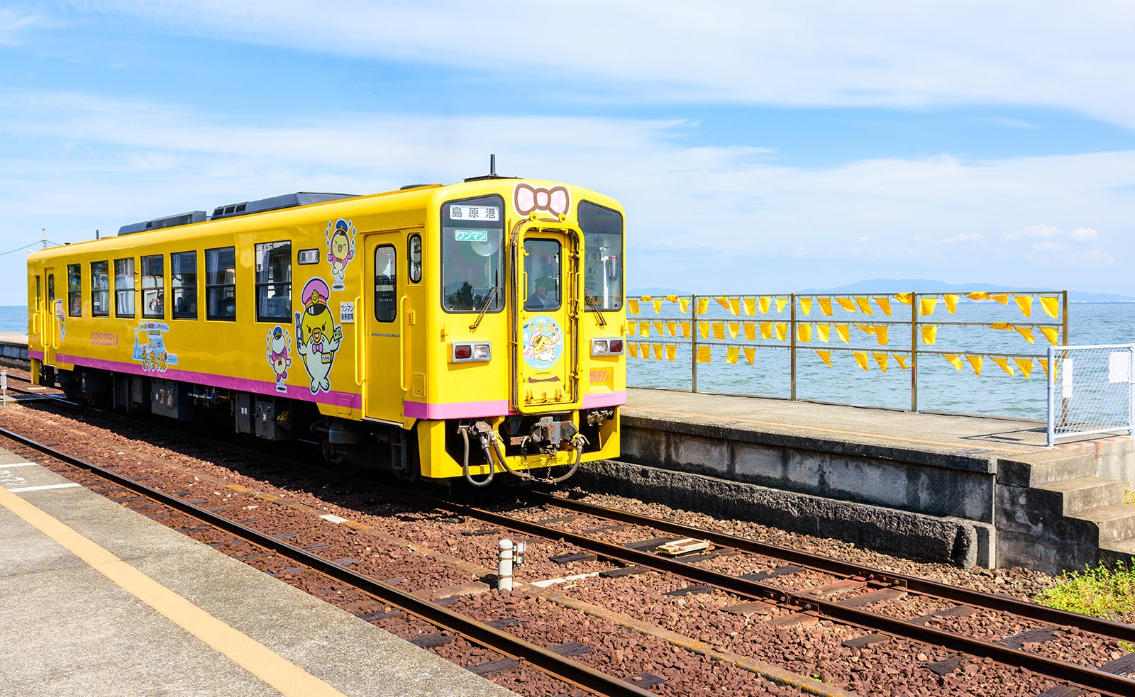 黄色いハンカチが飾られている駅を走る島原鉄道の黄色い列車風景