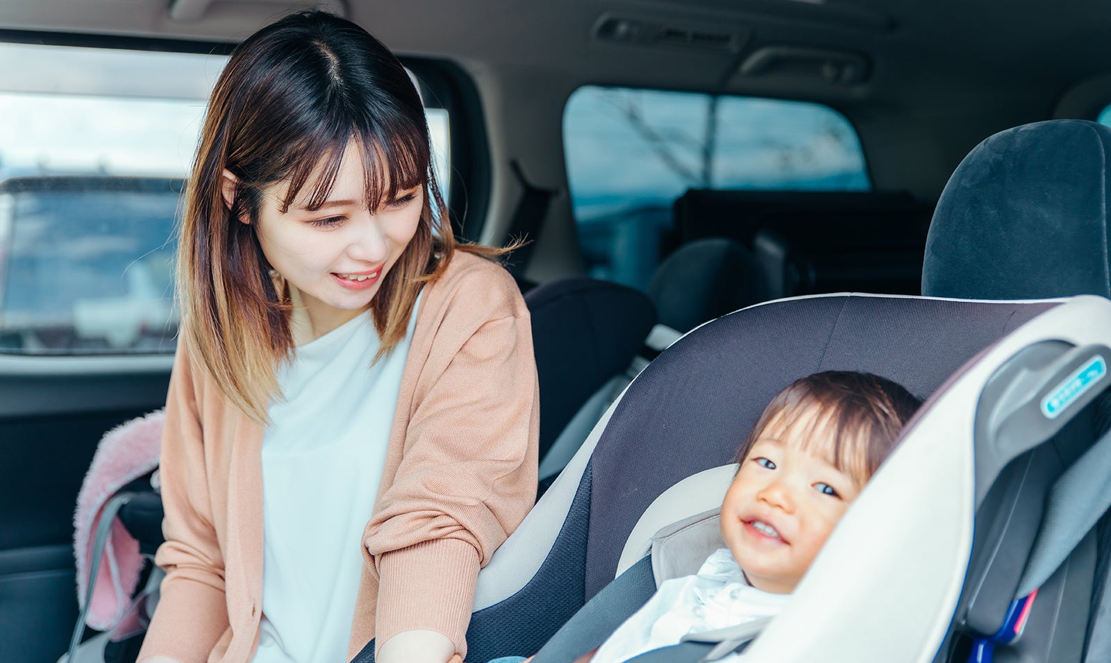 チャイルドシートに乗る子供を見つめる母親
