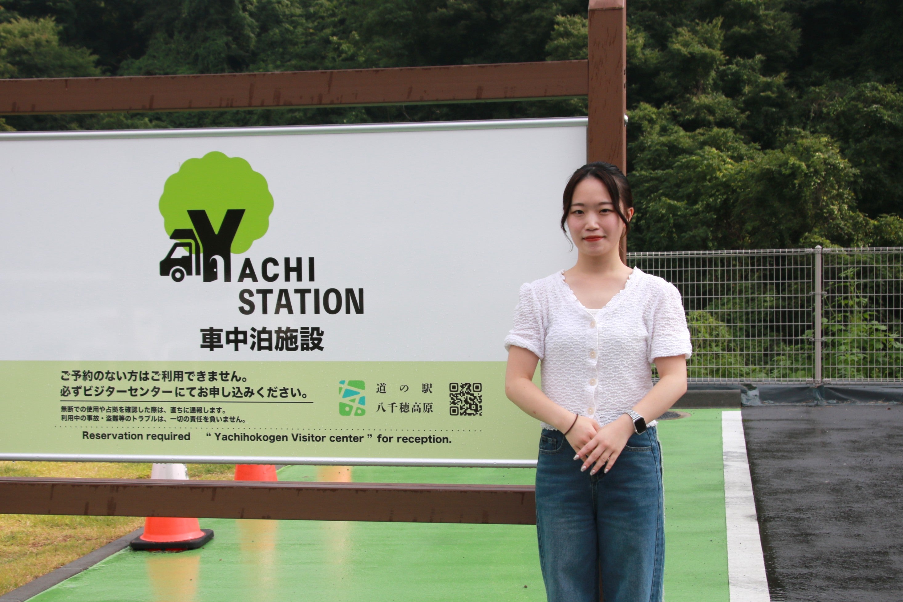車中泊施設看板の前でポーズをとる女性