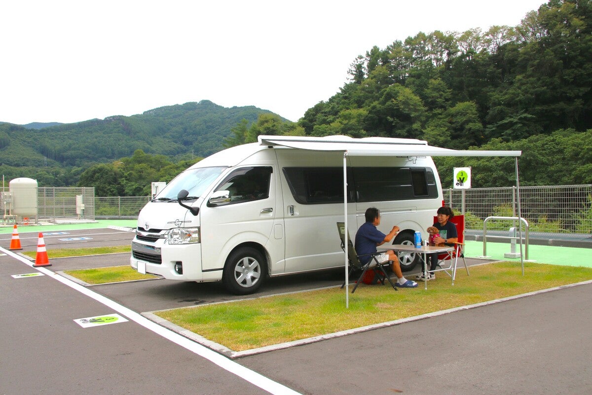キャンピングカーのサイドにテーブルと椅子を出しくつろぐ夫婦