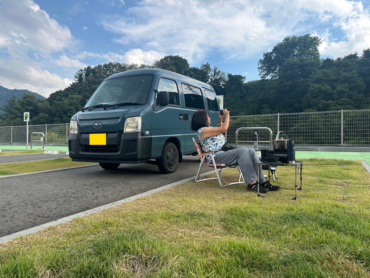 車中泊サイトの芝生スペースで椅子に座りくつろぐ女性