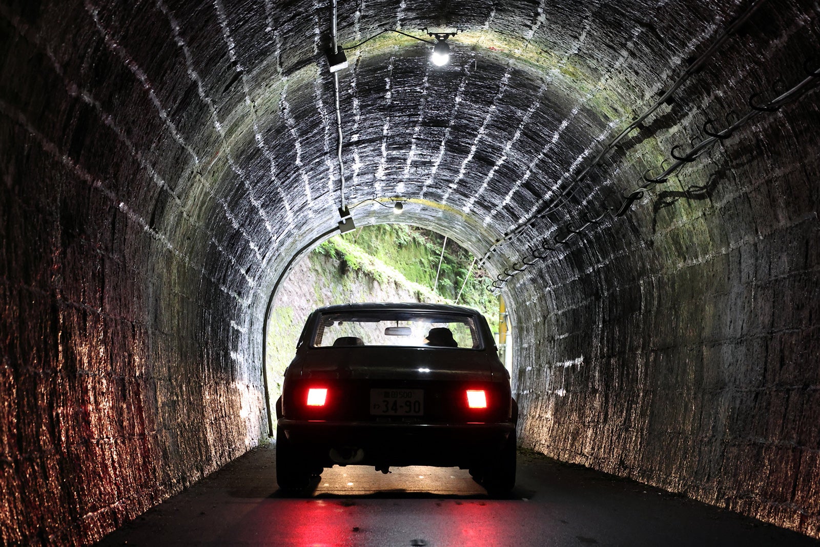 1974年式トヨタ・カローラレビンTE27型がヘッドライトに照らされた石造りトンネルを走行する後方ビュー。クラシックカー、旧車ドライブ、Vintage club by KINTO体験のイメージ