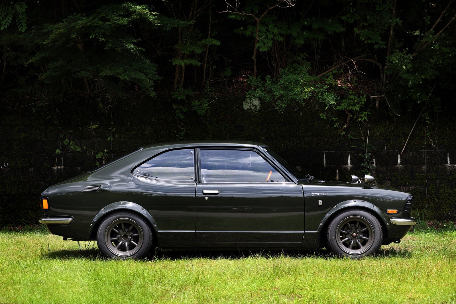 木々を背景に草地に停車するトヨタ・カローラレビンTE27型(1974年式・モスグリーン)のサイドビュー