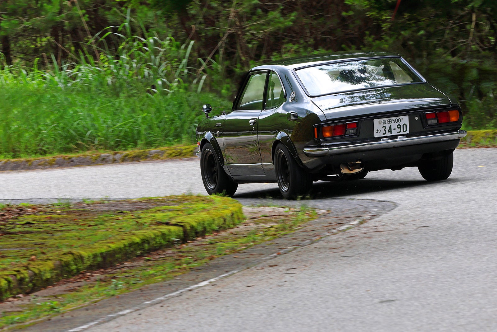 緑の中のカーブを走行するTE27型カローラレビンの後方ビュー。ナンバープレートは「わ 34-90」
