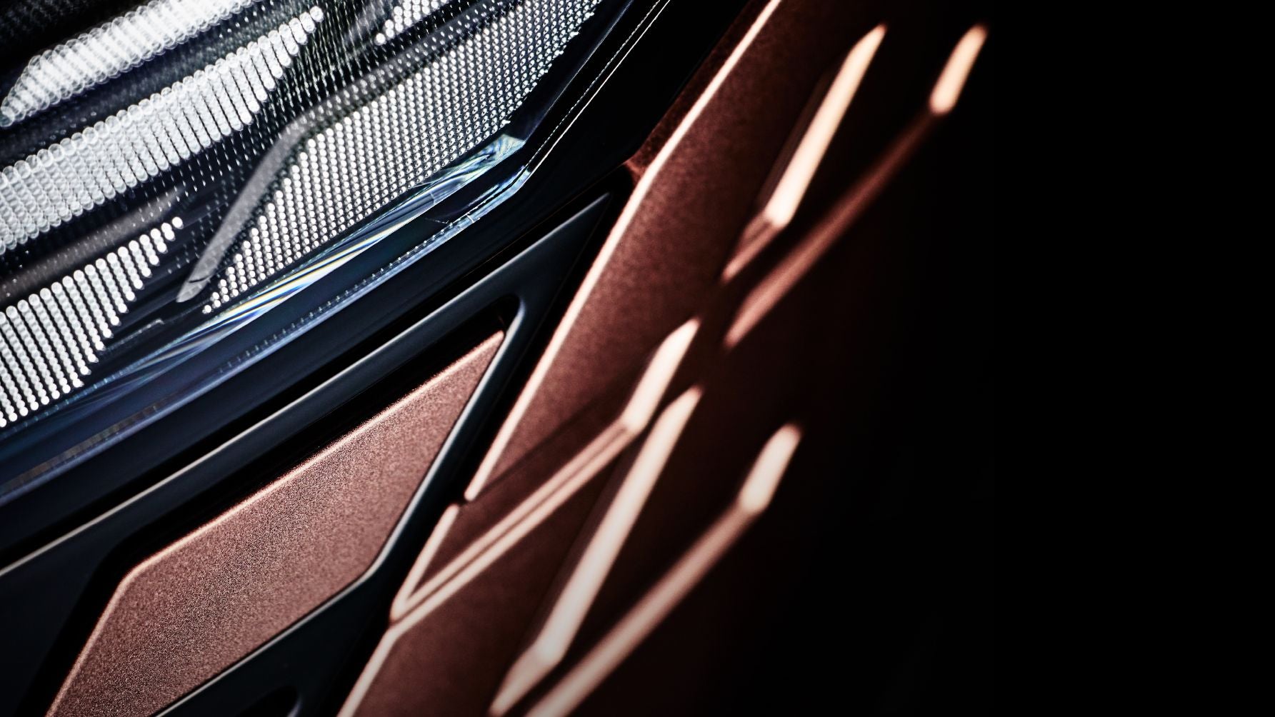 新型日産エルグランドのティザー画像。シャープなヘッドライトの一部と、車体表面に映る幾何学的な光と影のコントラストが強調されている。メタリックな質感と先進的なデザインが印象的なフロント部分のクローズアップ