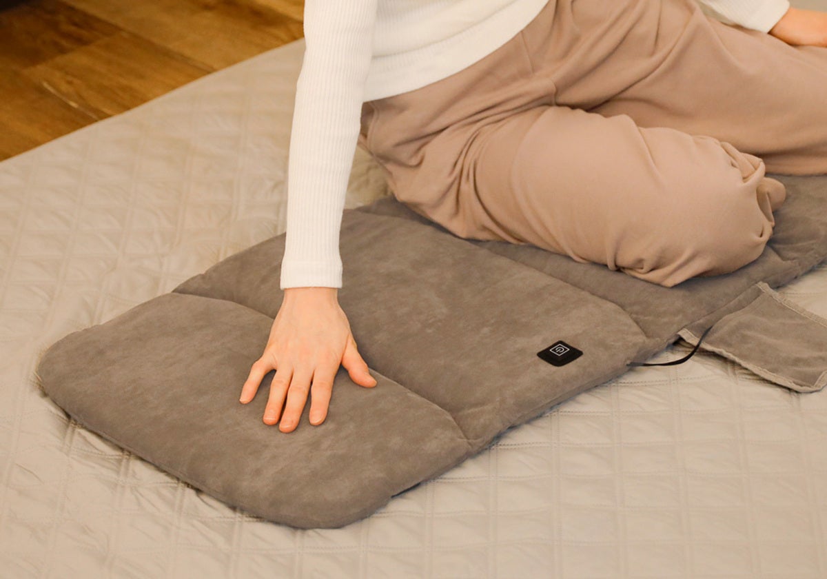 床に広げた電熱マットに座る女性