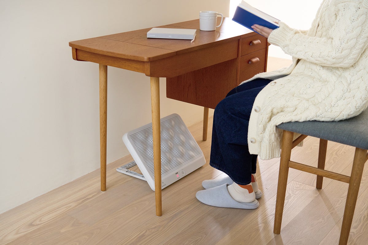 デスクの下にパネルヒーターを設置して温まる女性