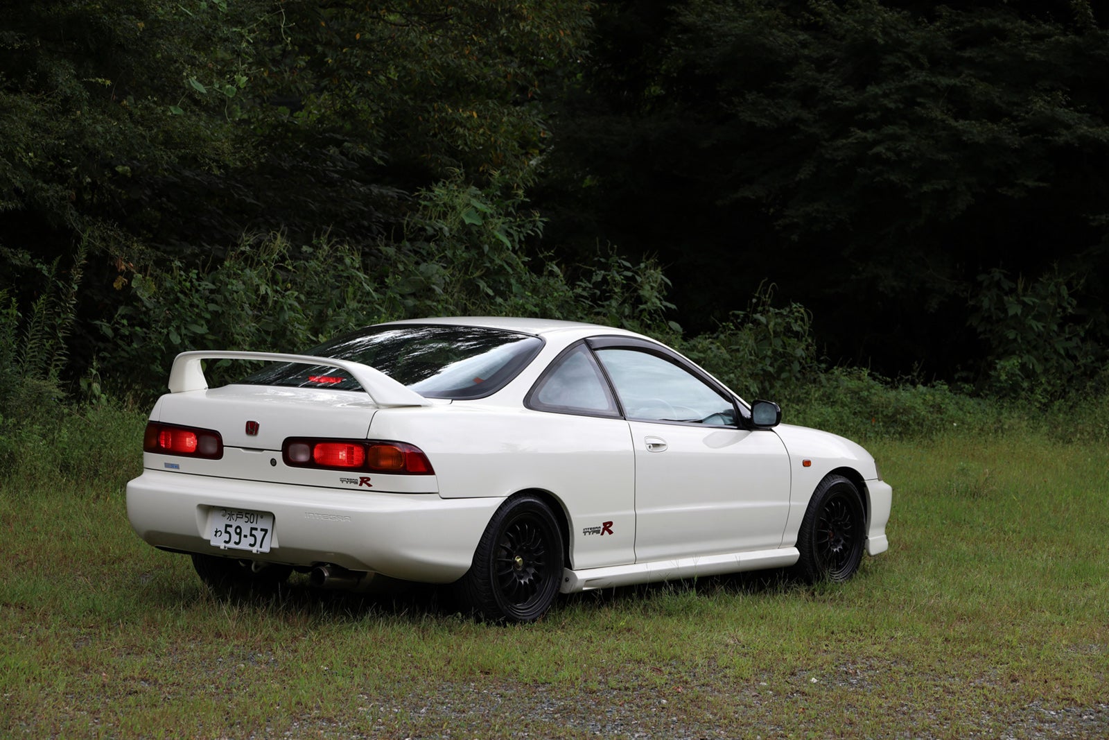 チャンピオンシップホワイトのホンダ・インテグラ タイプR（DC2）の正面写真。ヘッドライトを点灯し、緑豊かな場所に停車している