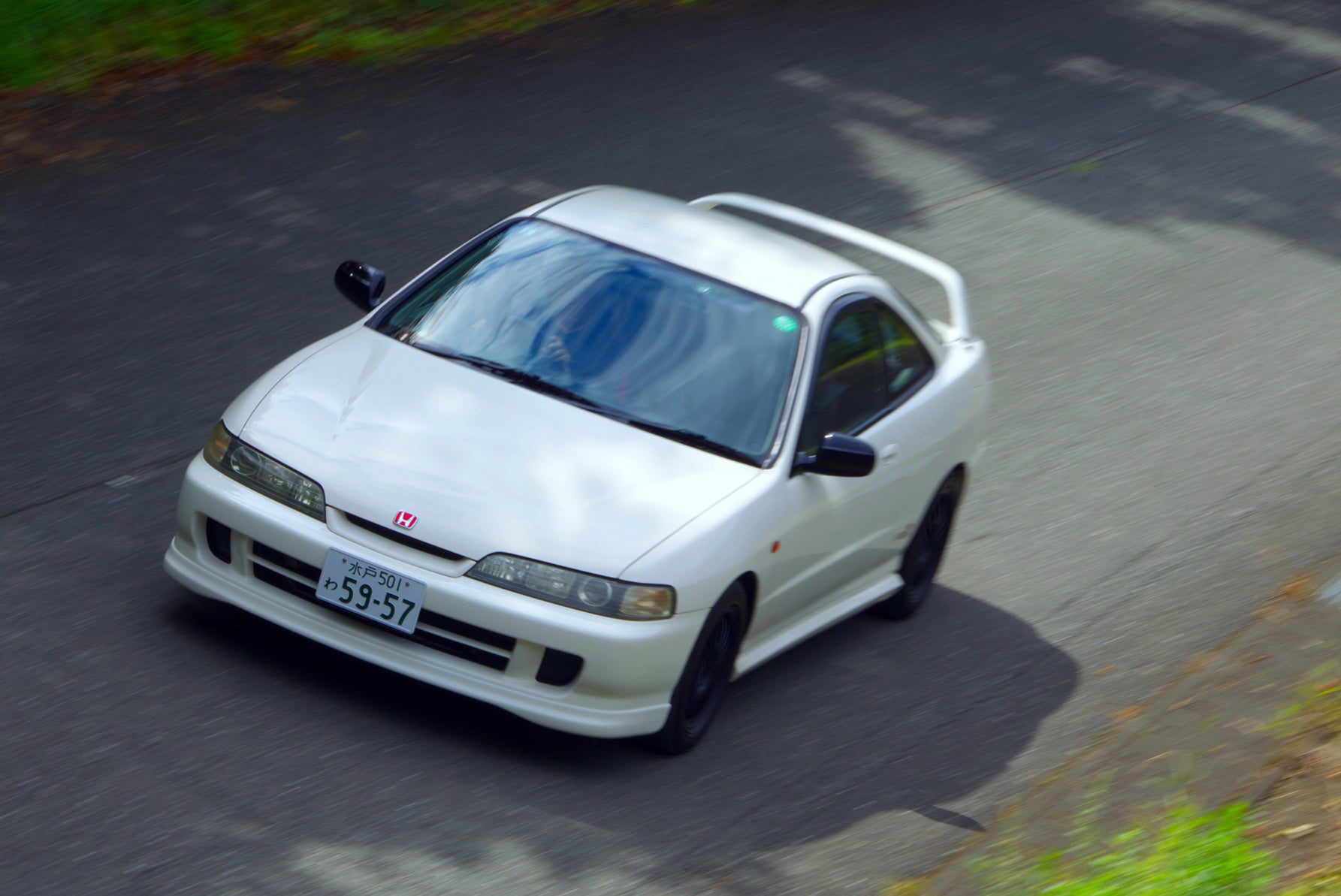 白いホンダ・インテグラタイプR（初代）がワインディングロードを走行する様子。フロントビューとサイドビューが見える