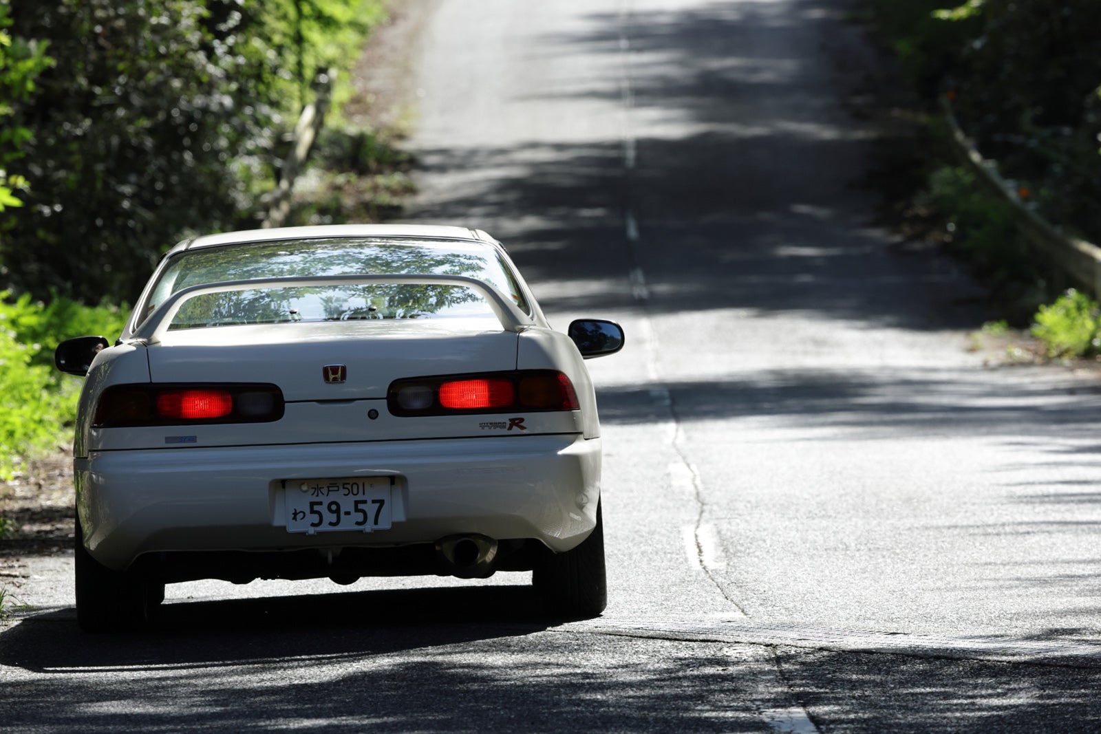 ホンダ インテグラ タイプR（初代）が山道を駆け抜ける後ろ姿。リアウイングとテールランプが印象的で、試乗レンタカーならではの走りの余韻を感じるシーン