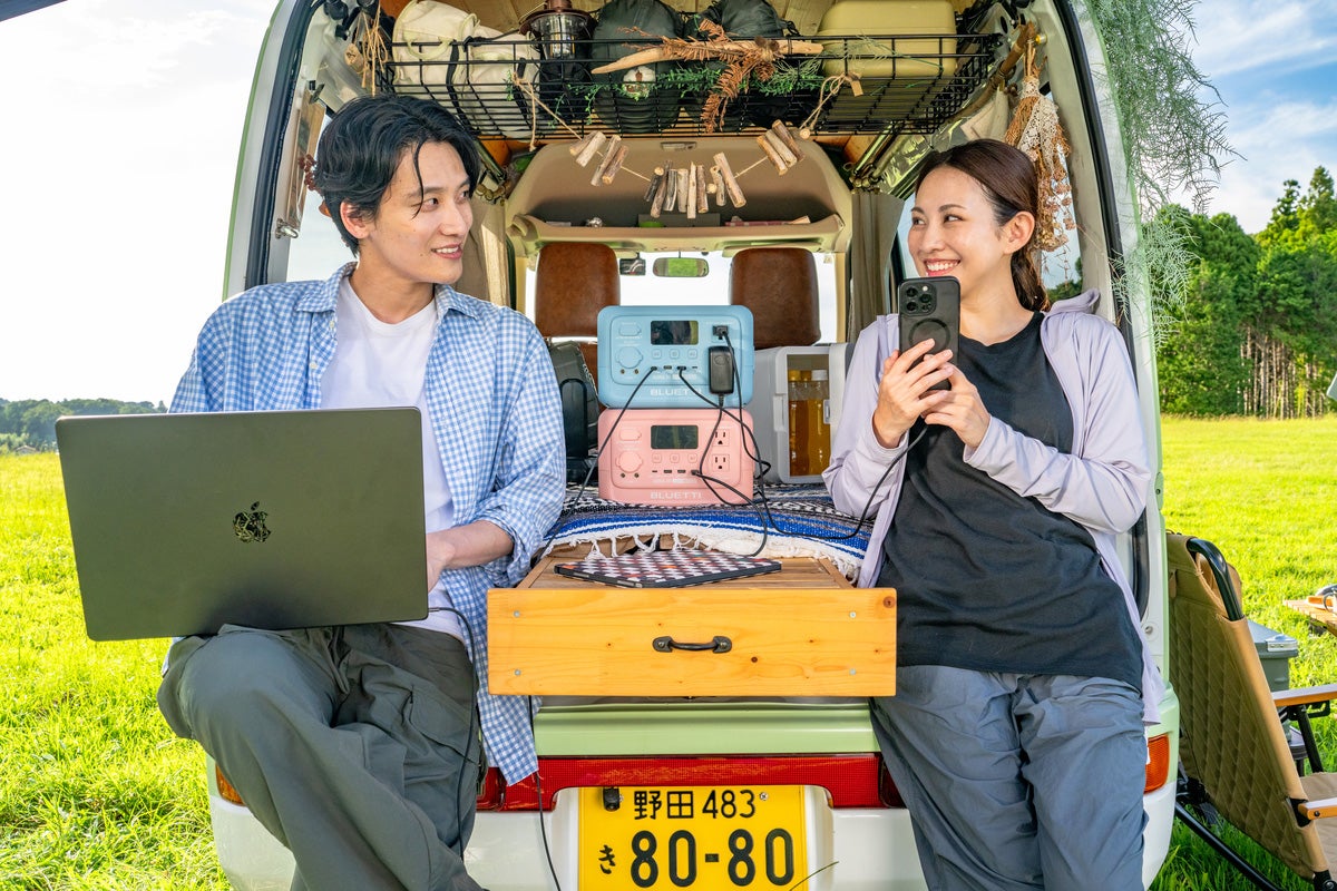 クルマのラゲッジに腰かけた男女と上下に重ねたポータブル電源