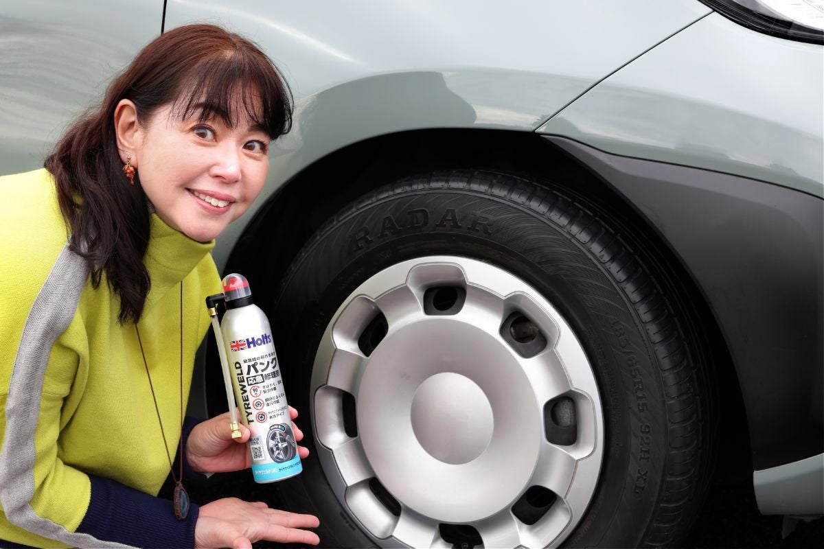 前輪タイヤの前でホルツのパンク修理剤を紹介しているモータージャーナリストの竹岡圭さん