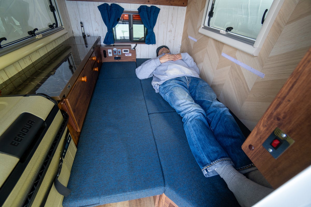 軽トラキャン車内でベッド展開し大人の男性が寝ころんでいる写真