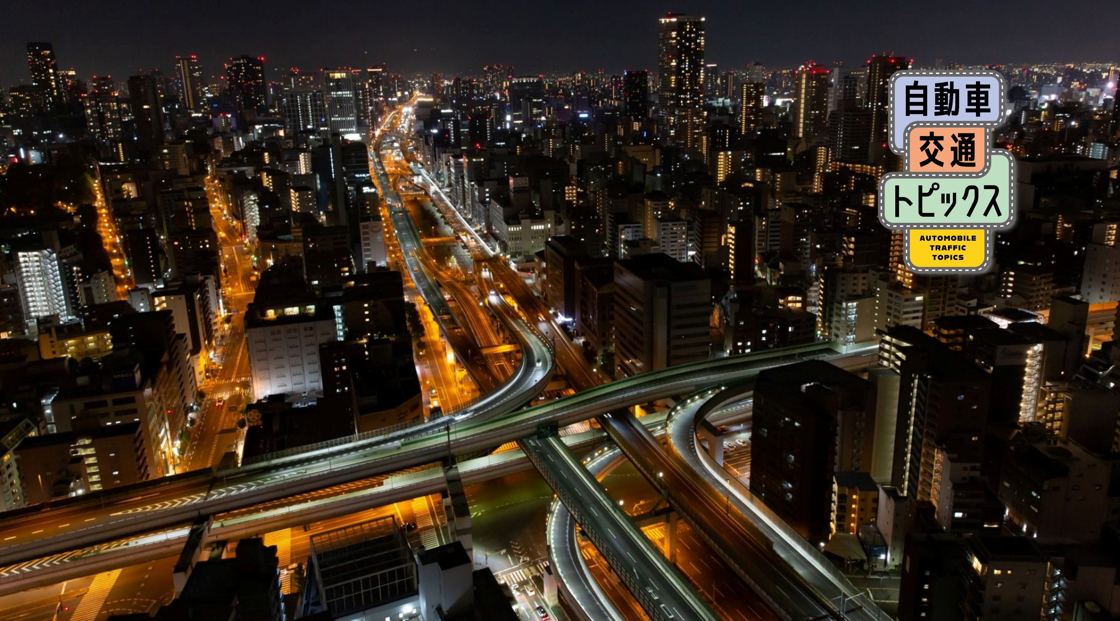 夜の高速道路を俯瞰したイメージ。ライトが連なる都市部の道路網と高層ビル群