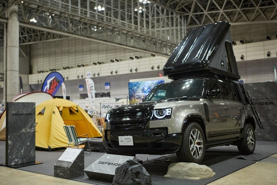幕張メッセ会場内のDefenderブース。屋根にルーフテントを展開したグレーのLand Rover Defenderが展示され、左奥には黄色いテントも設置されている