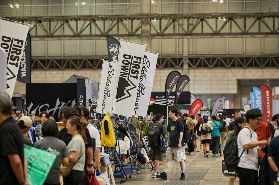 幕張メッセの広い展示ホール内に、FIRST DOWNやEDDIE BAUER、FEDECAなど複数のアウトドアブランドの幟旗が並び、多くの来場者が行き交っている