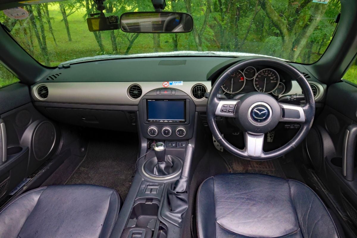 マツダ・ロードスター（NC型）のインパネ・運転席全景。黒を基調にシルバーのデコレーションパネルが配され、丸型のエアコン吹き出し口や5連メーター、MTのシフトノブが見える