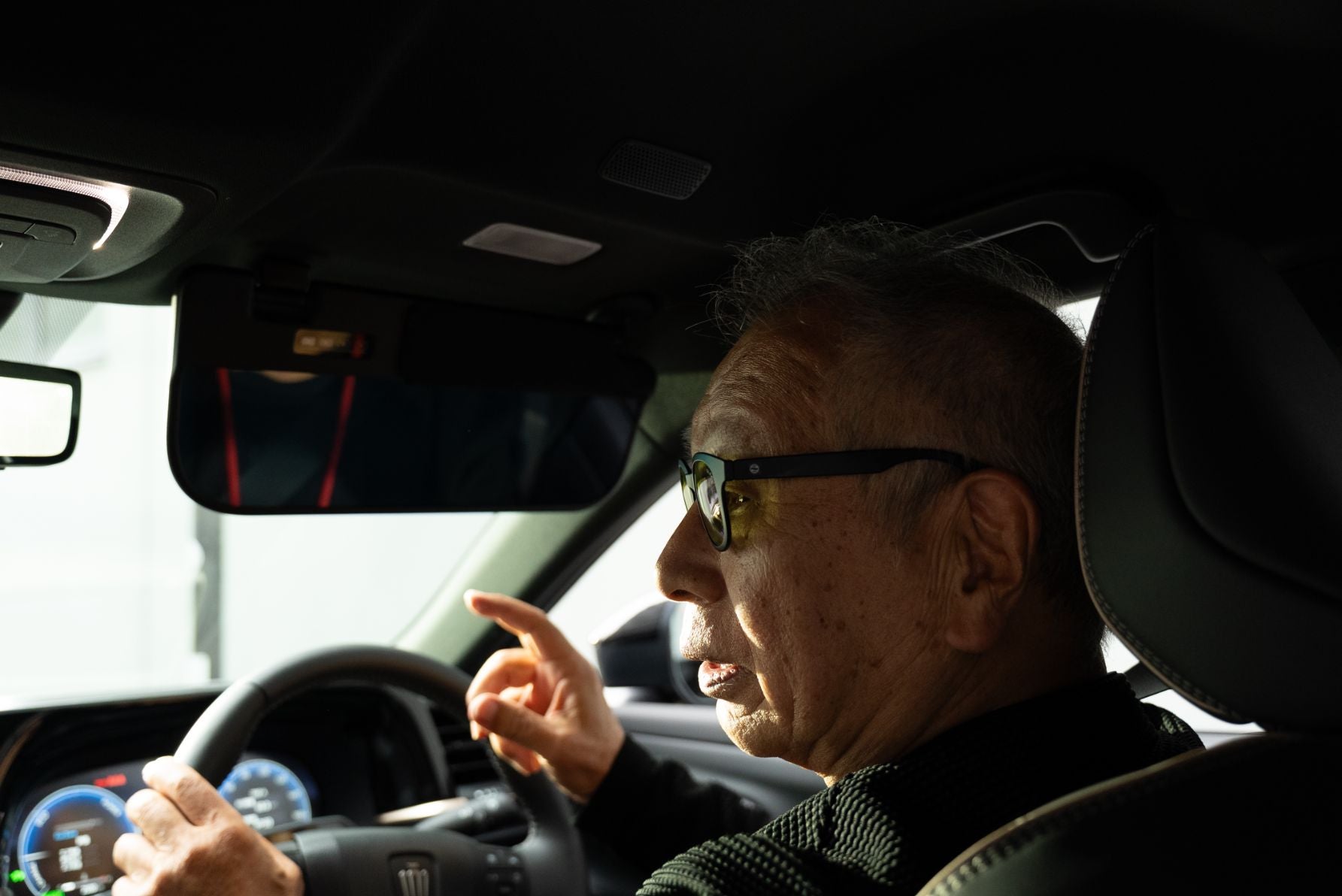デモカーの運転席で頭上の調光サンバイザーをチェックするモータージャーナリストの菰田潔氏