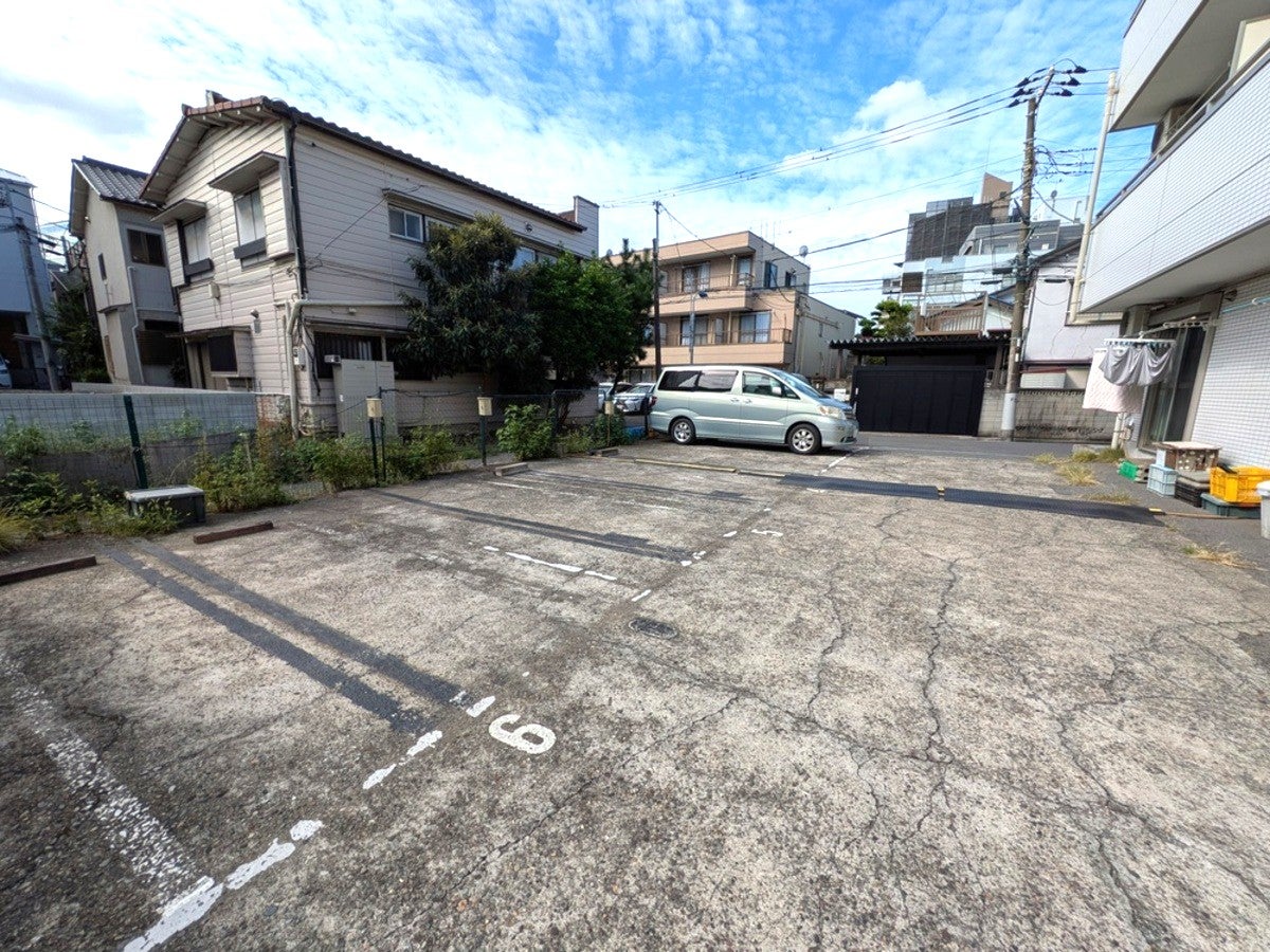 住宅街の中にあるコンクリート敷きの駐車場。区画番号が白線で描かれており、奥にミニバンが1台停まっている様子