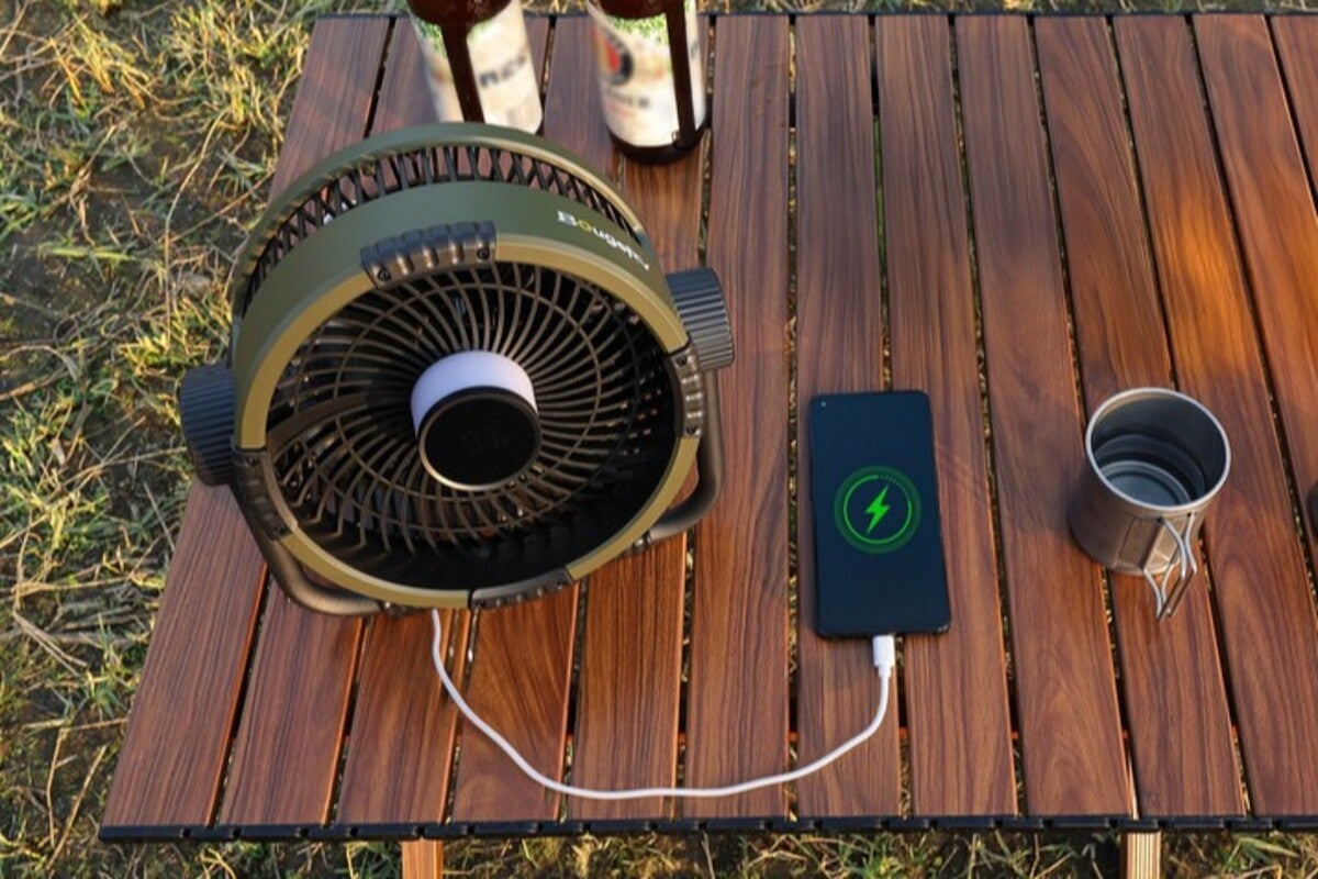 ウッドテーブル上でスマートフォンを充電しながら使っているカーキ色の扇風機
