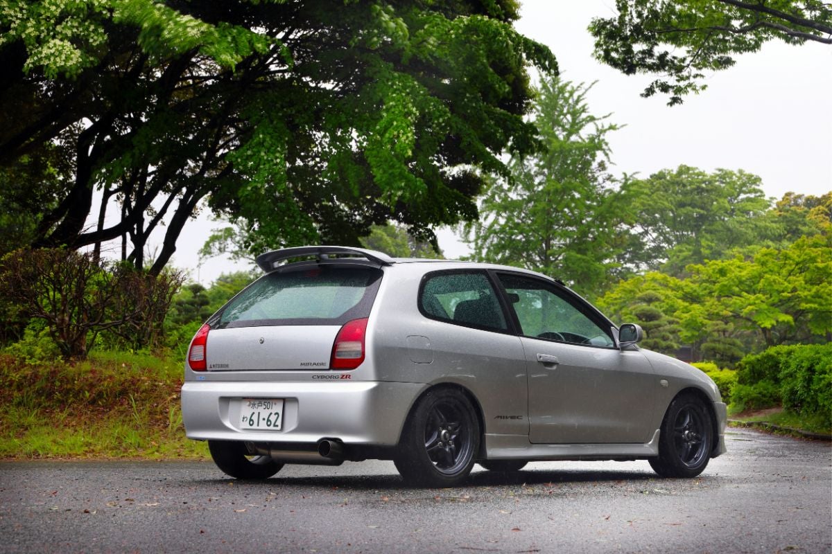 雨に濡れたアスファルトの上に停車している、シルバーの三菱ミラージュ サイボーグZR（E-CJ4A型）を右斜め後方から捉えた写真