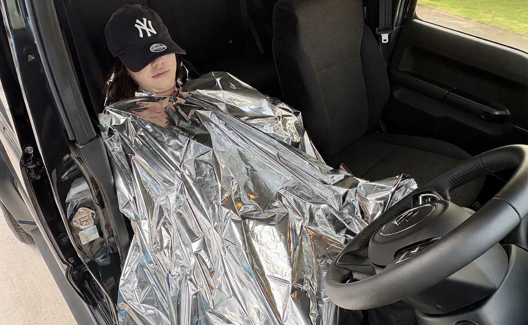 簡易保温アルミポンチョを着て車内で寝ている写真