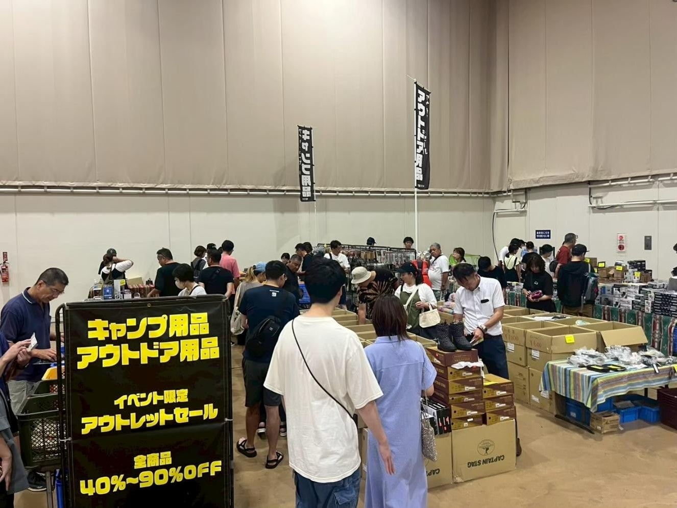 キャンプ用品やアウトドア用品が並ぶ販売コーナーを見る来場者