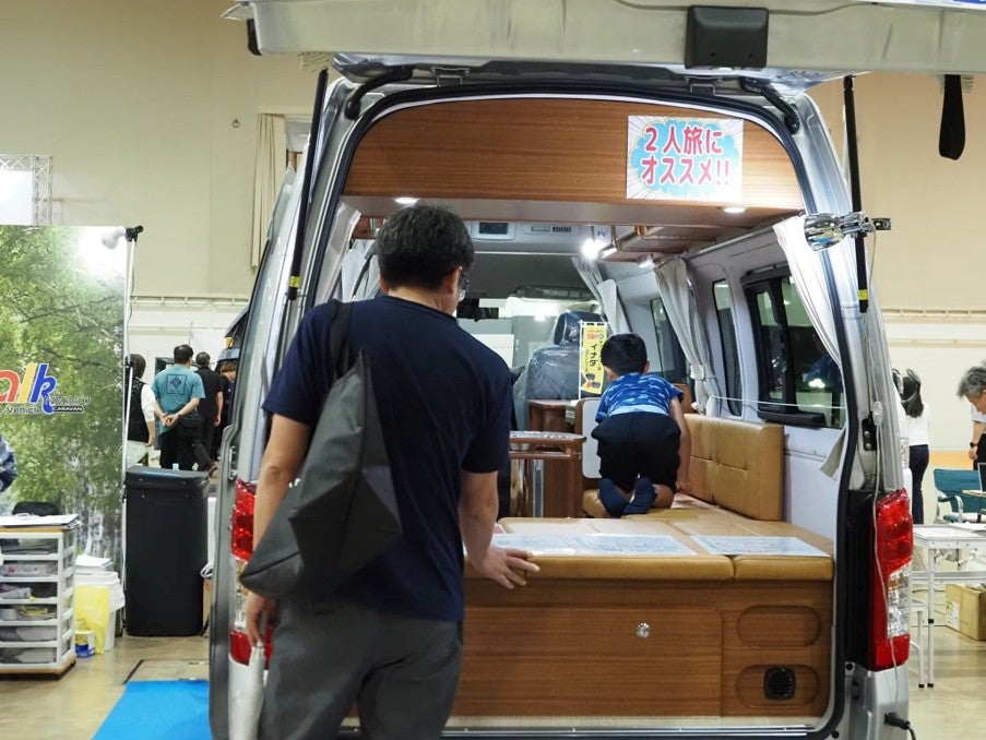 キャンピングカーの後部から車内のベッドスペースを見学する親子