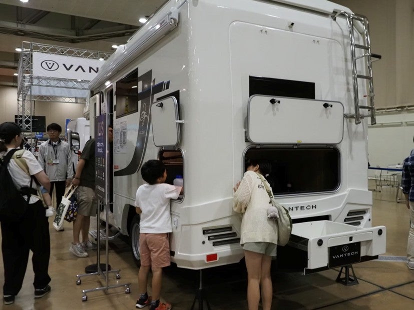 VANTECHのキャンピングカーの後部ドアから、荷物の積み下ろし口や車内を親子でのぞき込む様子