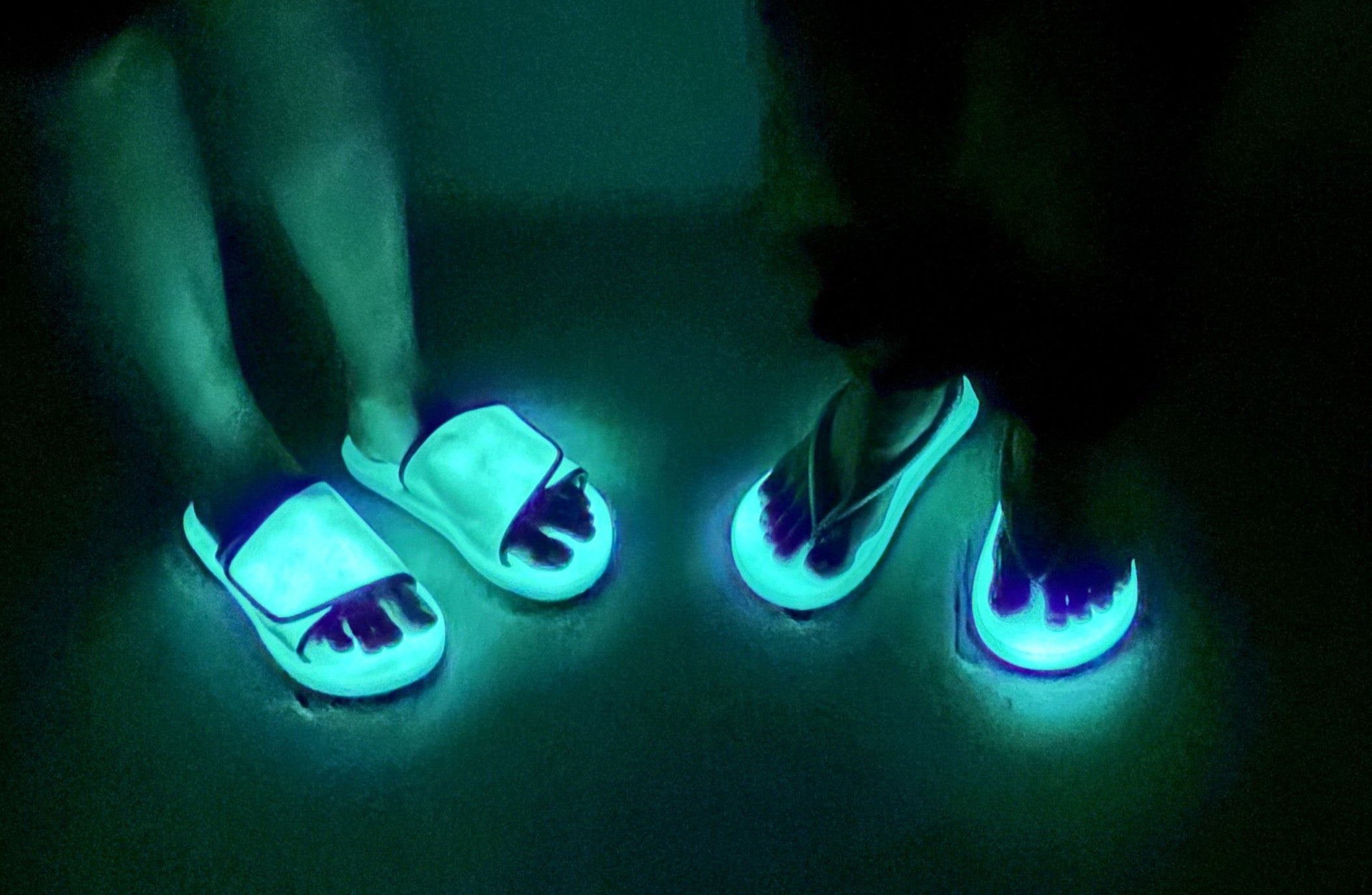 暗闇の中で蓄光サンダル「waraji sandal glow」と「Slide glow」を履いて佇む2人の足元