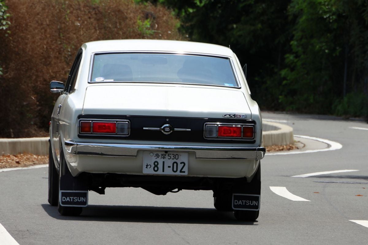 ワインディングロードを走行する白いサニークーペのリアビュー