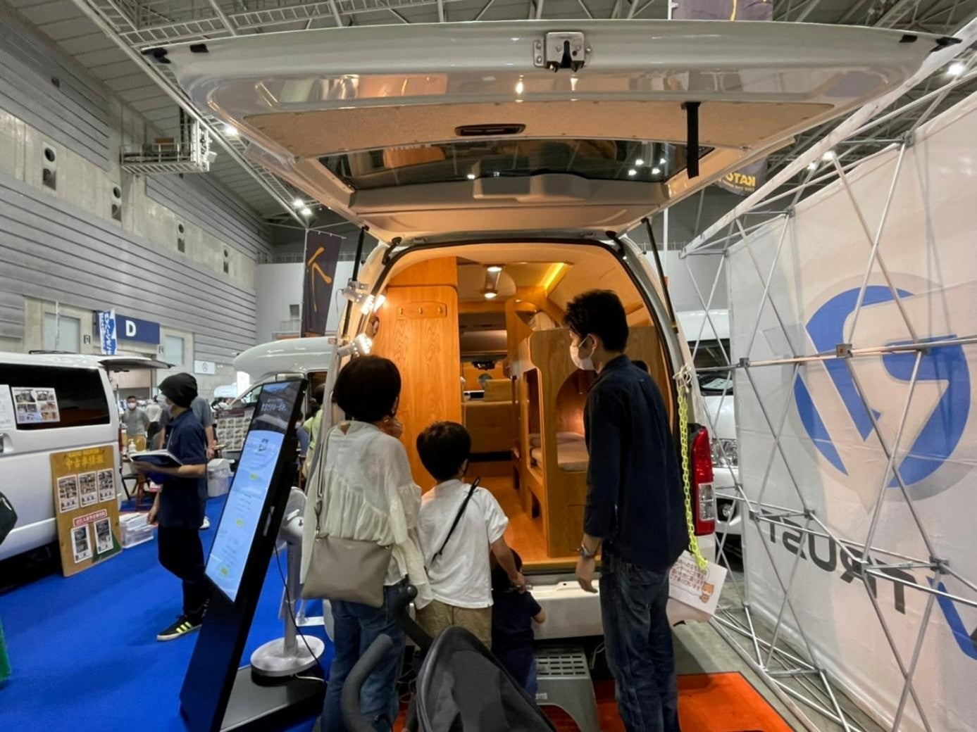屋内の展示ブースに複数のキャンピングカーが並び、来場者が車両を見学する様子