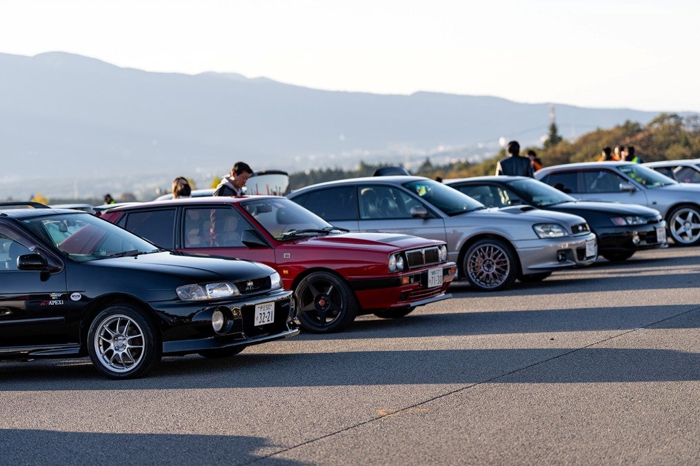 過去開催のハチマルミーティングで、1980～90年代の国産車が駐車場に並ぶ様子