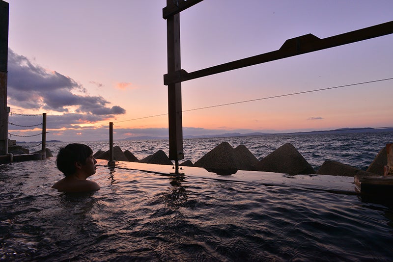 夕暮れ時に海のそばにある露天風呂につかる男性