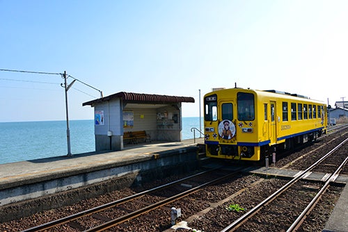 海沿いの駅のホームから走り去っていく黄色い電車