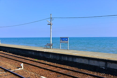 電車の線路と、その奥に広がる青い海と空