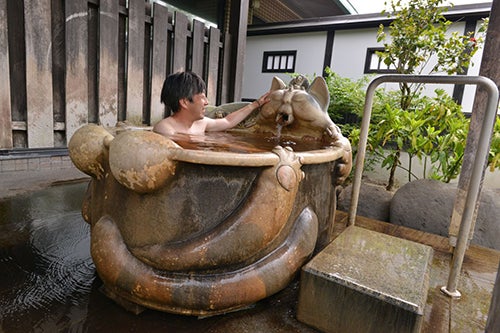 猫をモチーフに作られた陶器風呂に入る男性