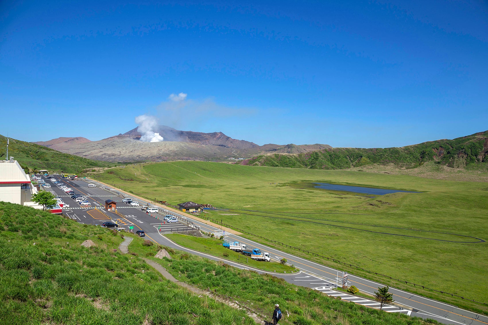 写真3 草千里から道路を挟んで向かい側に広い駐車場がある。遠くには阿蘇山の火口が見える（撮影エリアは地図３を参照）