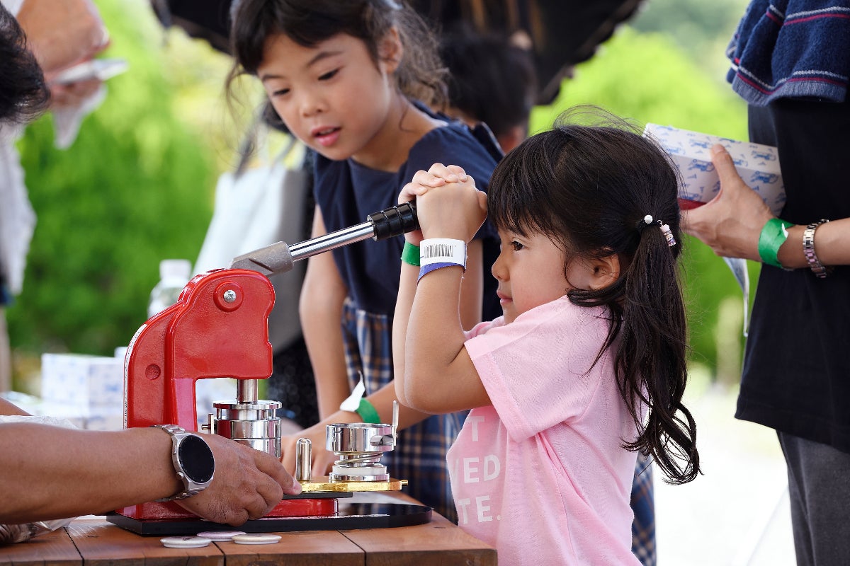 缶バッジを作る機械のレバーを引く子供たち