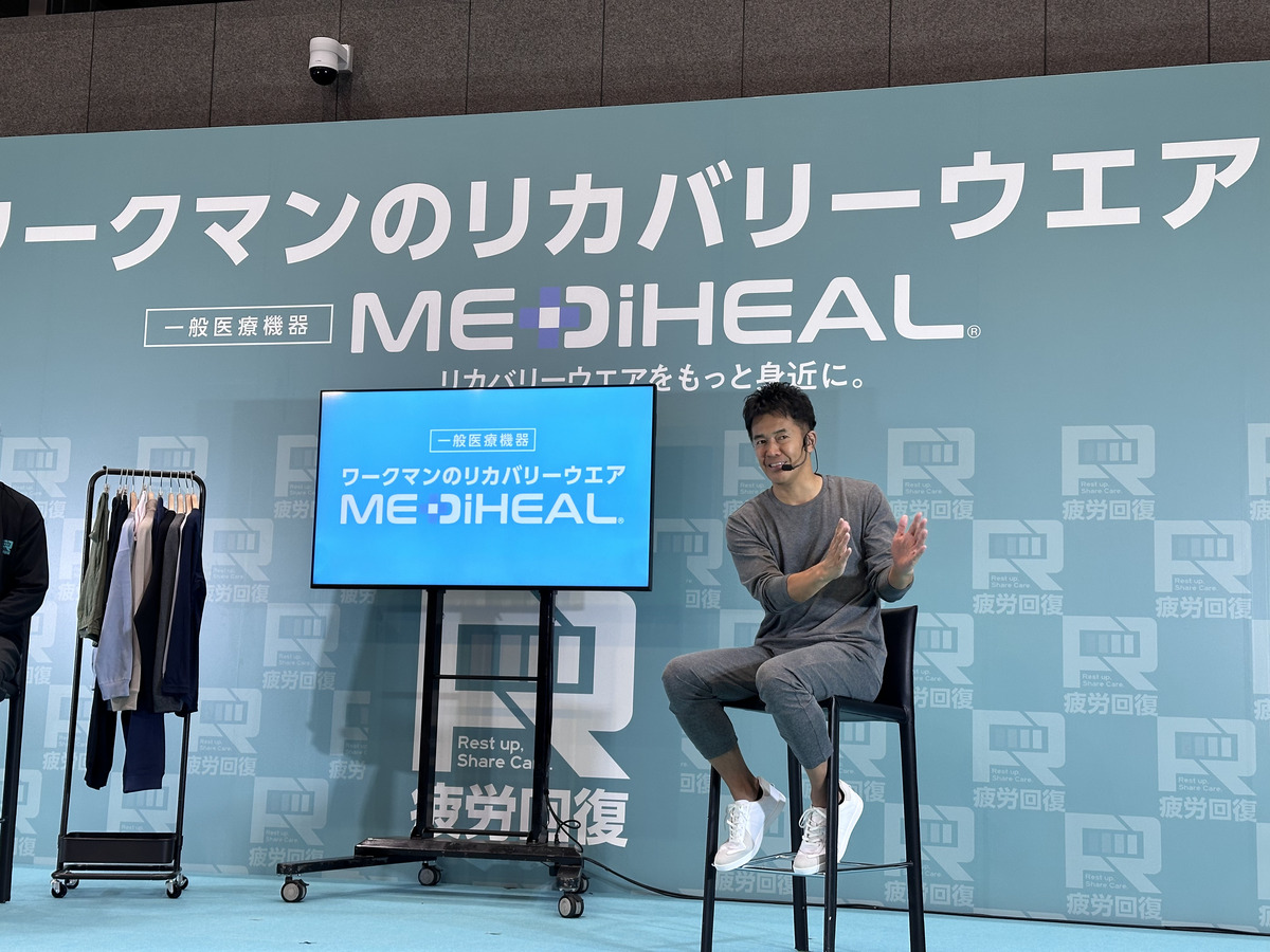 リカバリーウエアを着用し椅子に腰かけてトークショーをする武井壮