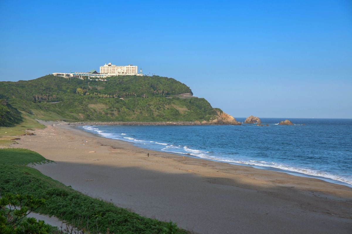 伊良湖岬近くの恋路ヶ浜を撮影した風景。穏やかな波が打ち寄せる砂浜と、背景には緑の丘の上に建つホテルが見える