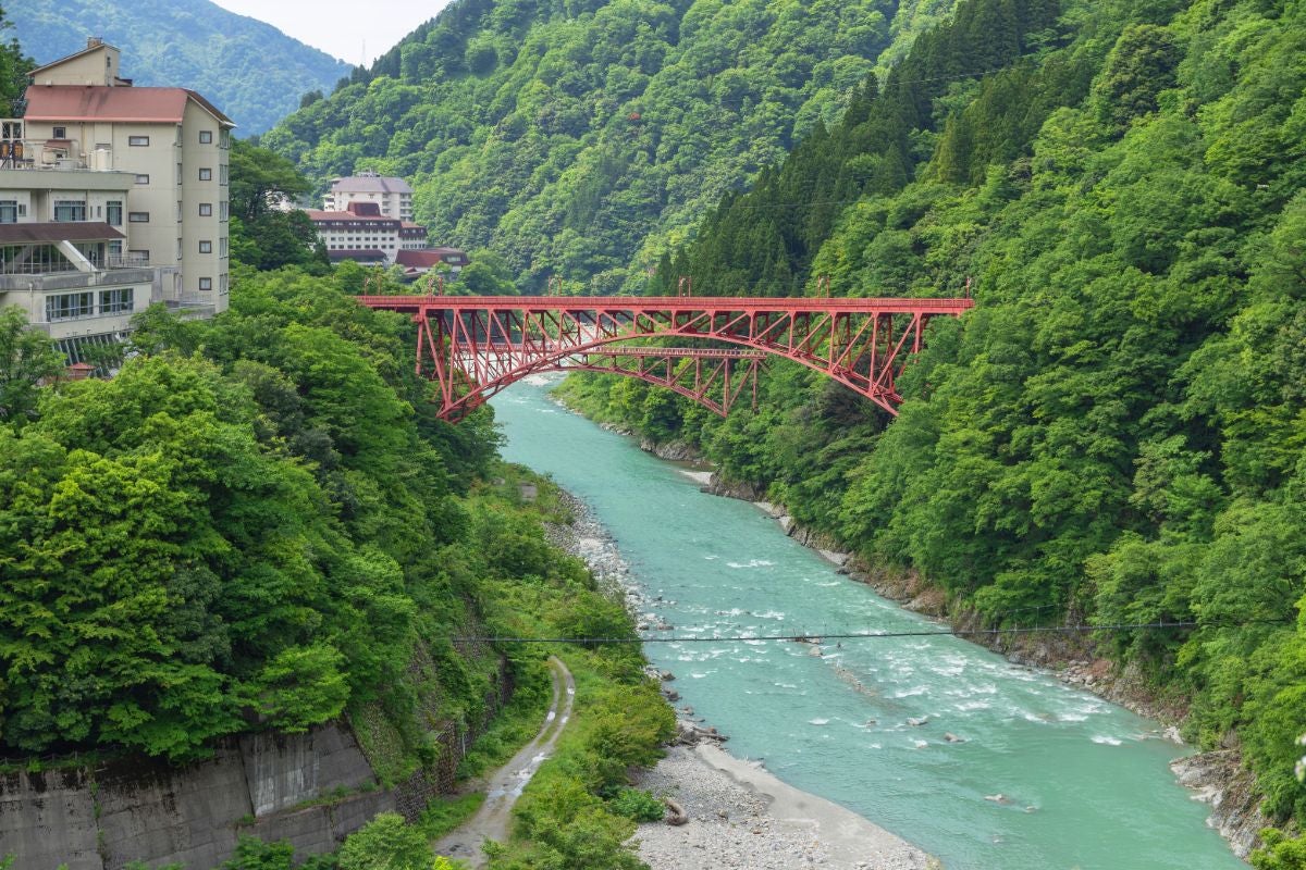 黒部峡谷鉄道の新山彦橋と、エメラルドグリーンに輝く黒部川が織りなす富山の絶景スポット。周囲の深い緑が峡谷の雄大さを引き立てる