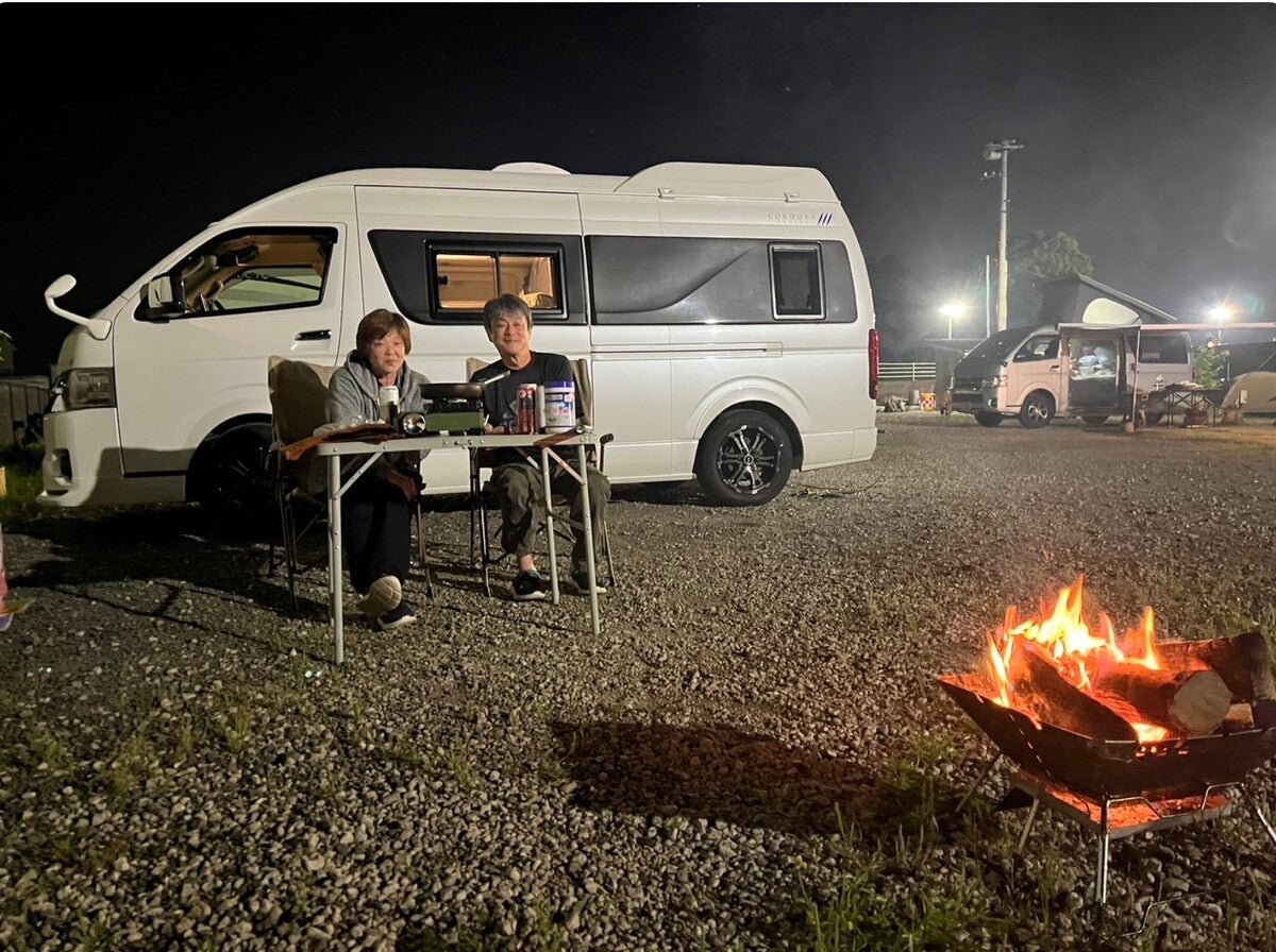 車中泊サイトでクルマをバックに焚き火を楽しむ夫婦
