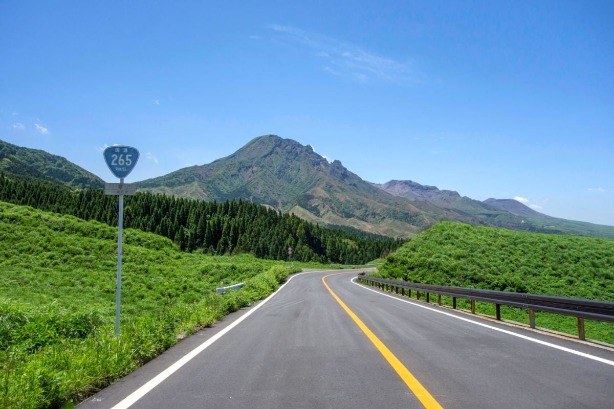 阿蘇・国道265号から望む根子岳、青空の下に続くワインディングロードと緑の草原が広がる絶景ドライブコース