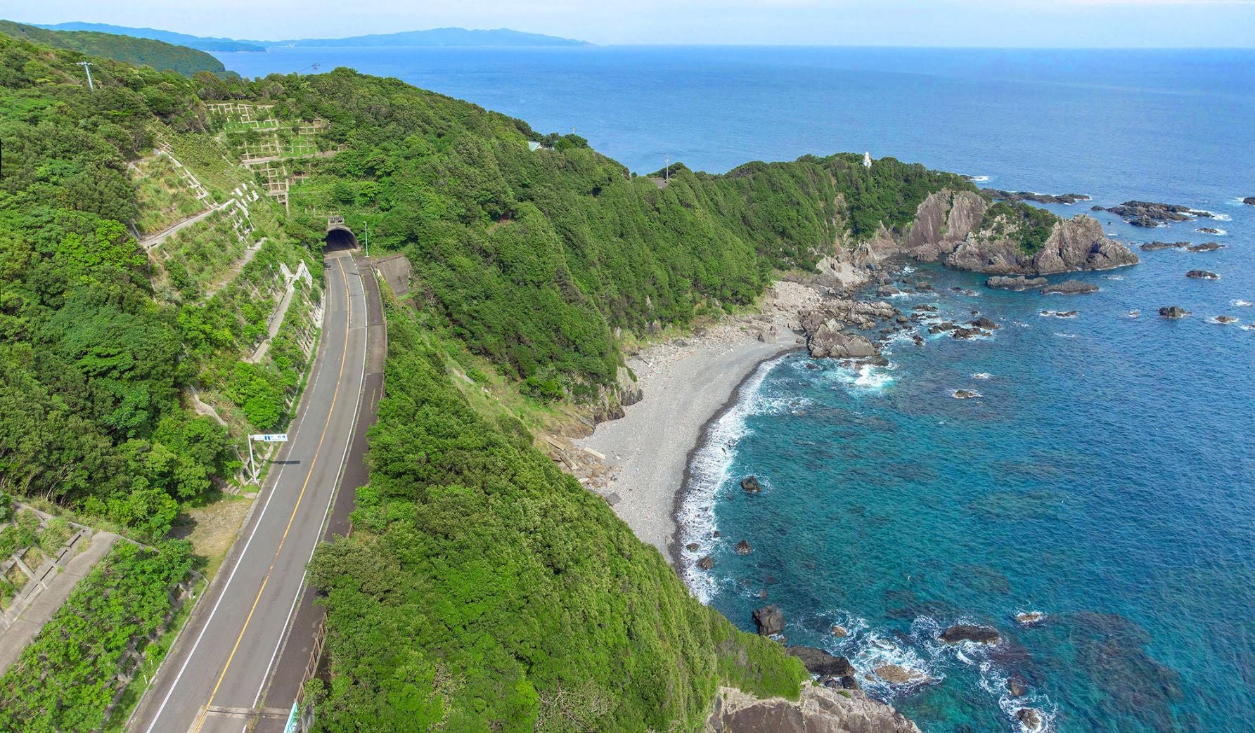 高知県足摺サニーロードの空撮写真。左側に緑に囲まれた道路と叶崎トンネル、右側には岩場と青く澄んだ太平洋が広がっている