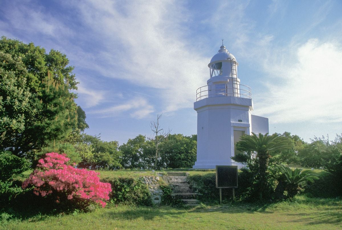 高知県叶崎灯台の写真。白い八角形の灯台が青空の下、緑の木々と花に囲まれて立っている
