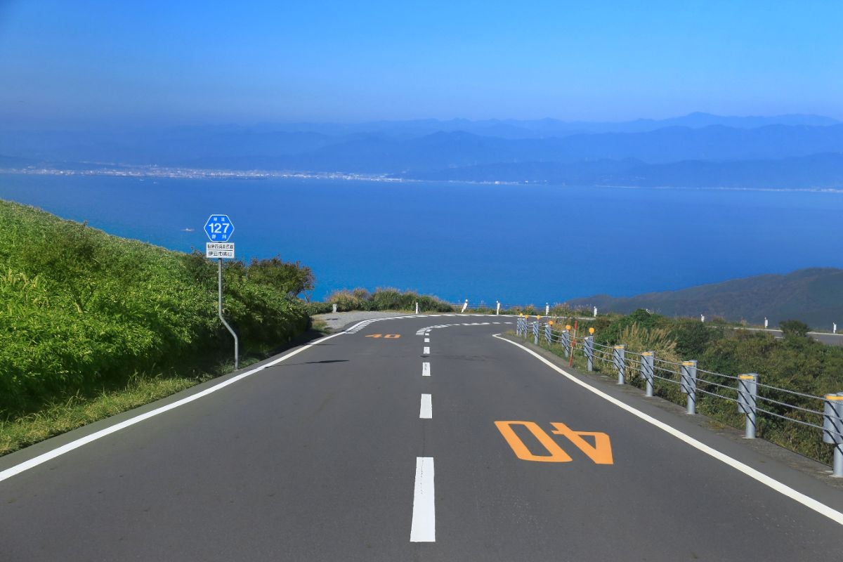 西伊豆スカイラインの舗装道路から見える駿河湾の青い海と対岸の街並み。視界いっぱいに広がる海景