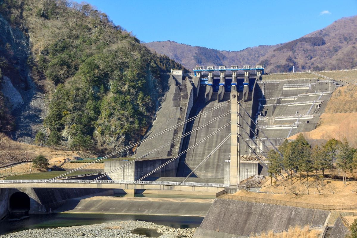 丹沢湖の巨大なダムの堤体。コンクリート製の堤体にはゲートや放流設備が見え、その手前には湖水が貯えられている。周囲は山々に囲まれている。